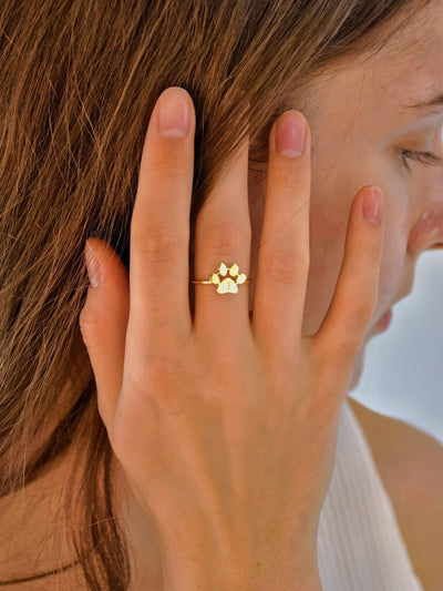 Close-up of a hand wearing a gold paw print ring with a blurred background