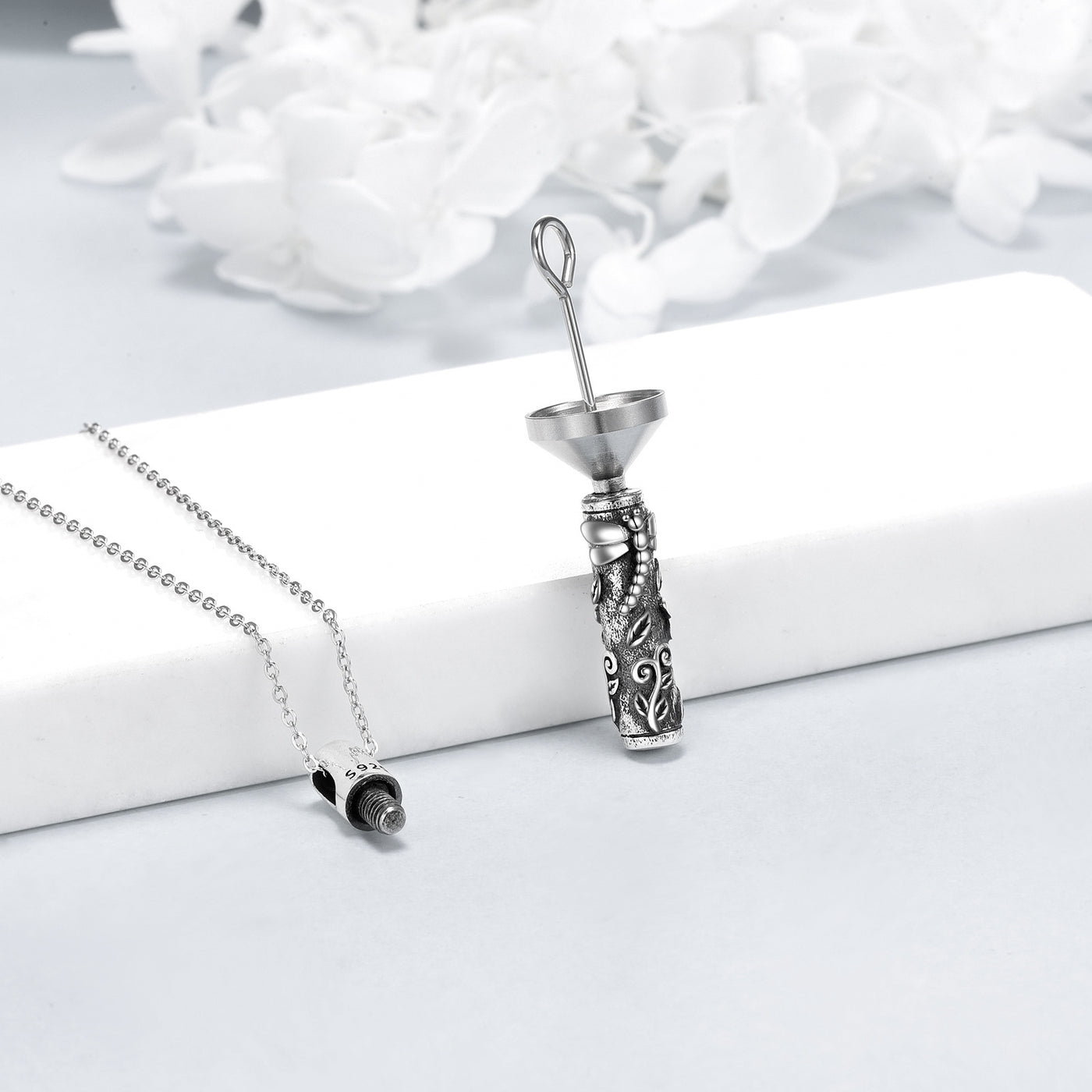 Silver necklace with a detailed pendant on a white surface with a floral background