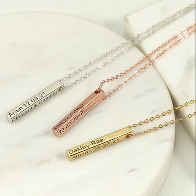 Three personalized bar necklaces on a marble surface