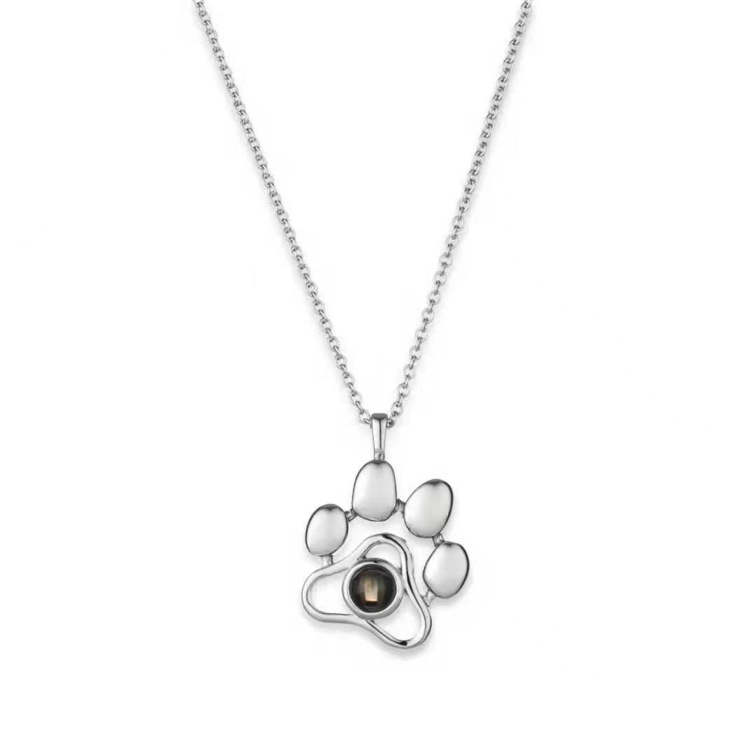 Silver paw print necklace with a central gemstone on a white background