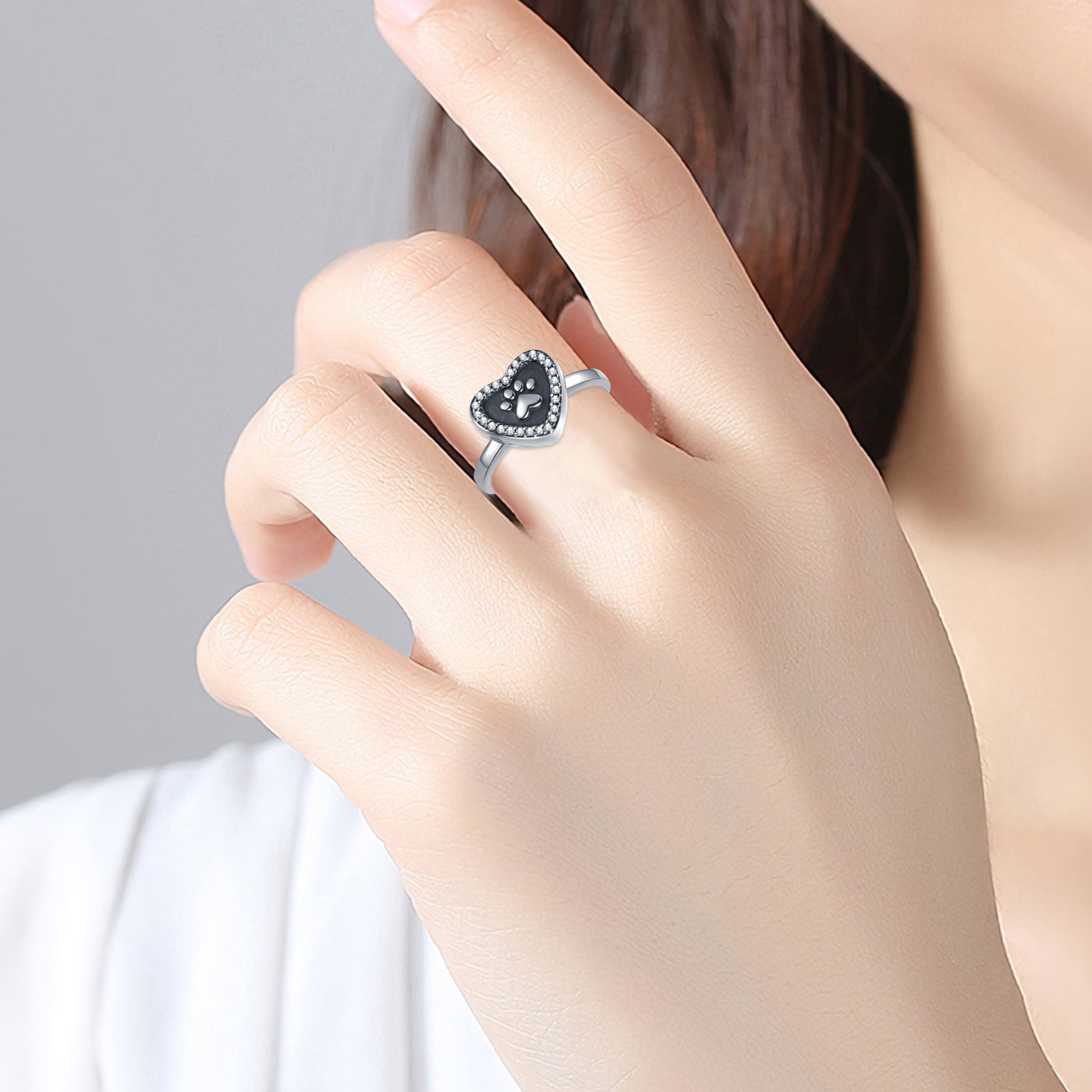 Heart-shaped ring with black gemstone on a hand against a neutral background