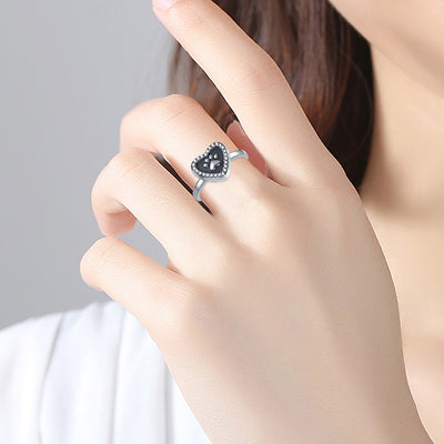 Heart-shaped ring with black gemstone on a hand against a neutral background