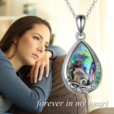 Woman sitting on a couch with a colorful teardrop pendant necklace in front of her.