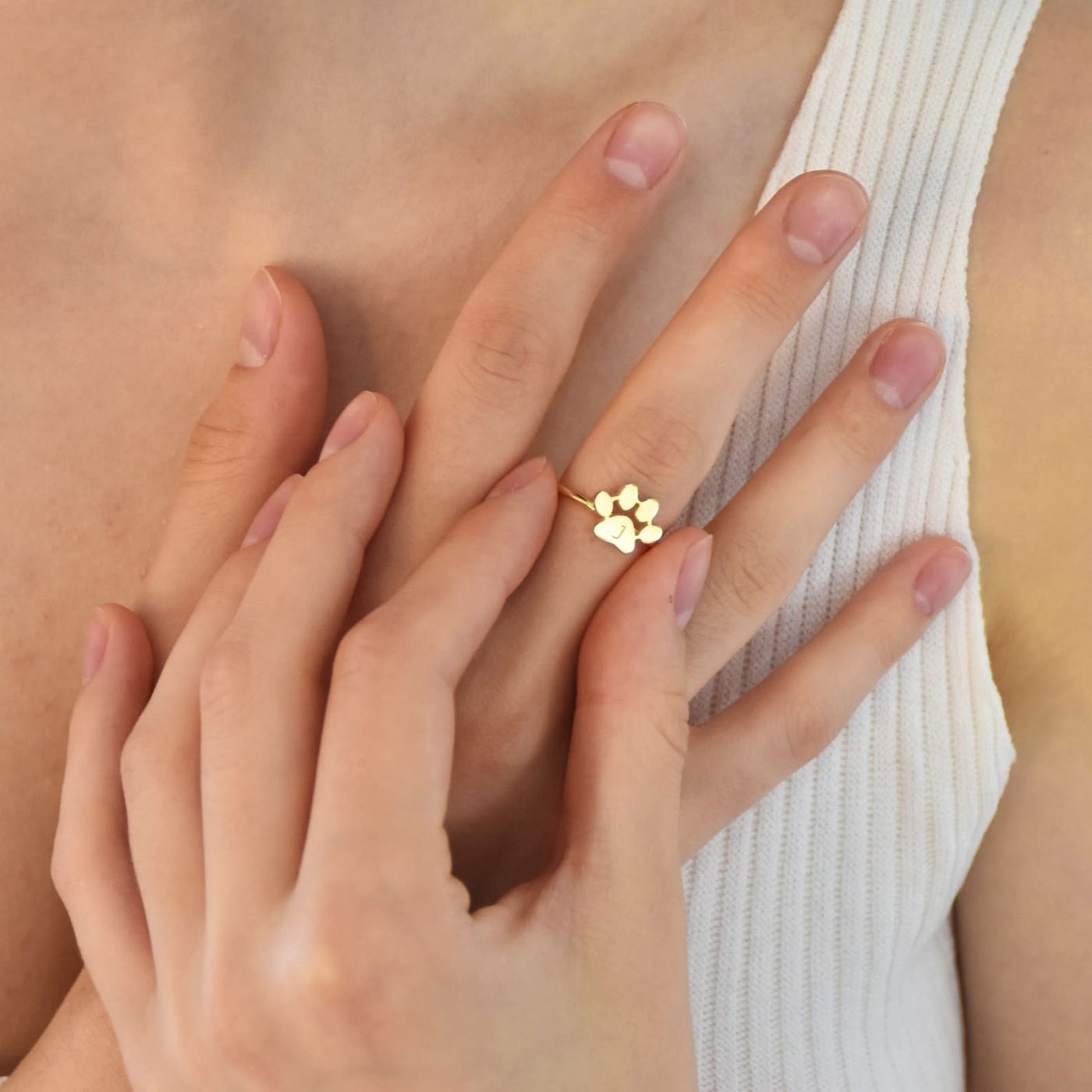 Gold paw print ring on a person's finger with a soft background