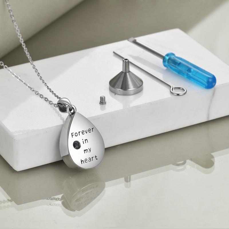 Teardrop-shaped pendant necklace with 'Forever in my heart' engraving on a white surface with tools.