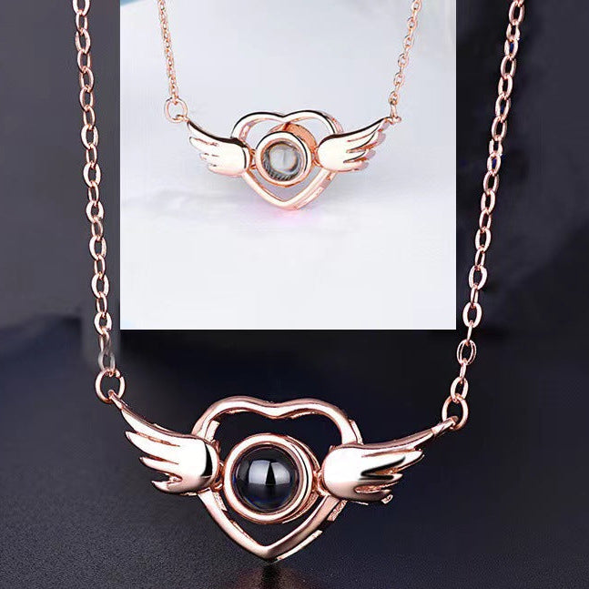 Rose gold necklace with heart and wings design on a dark background