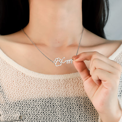 Person holding a silver necklace with a paw print and name 'Coppy' inscription.