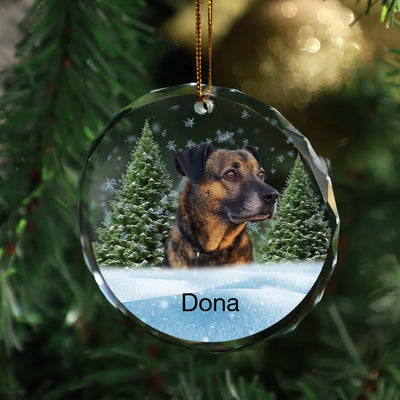 Circle-shaped glass ornament featuring a photo of a dog, surrounded by a winter forest scene, ideal as a pet memorial keepsake