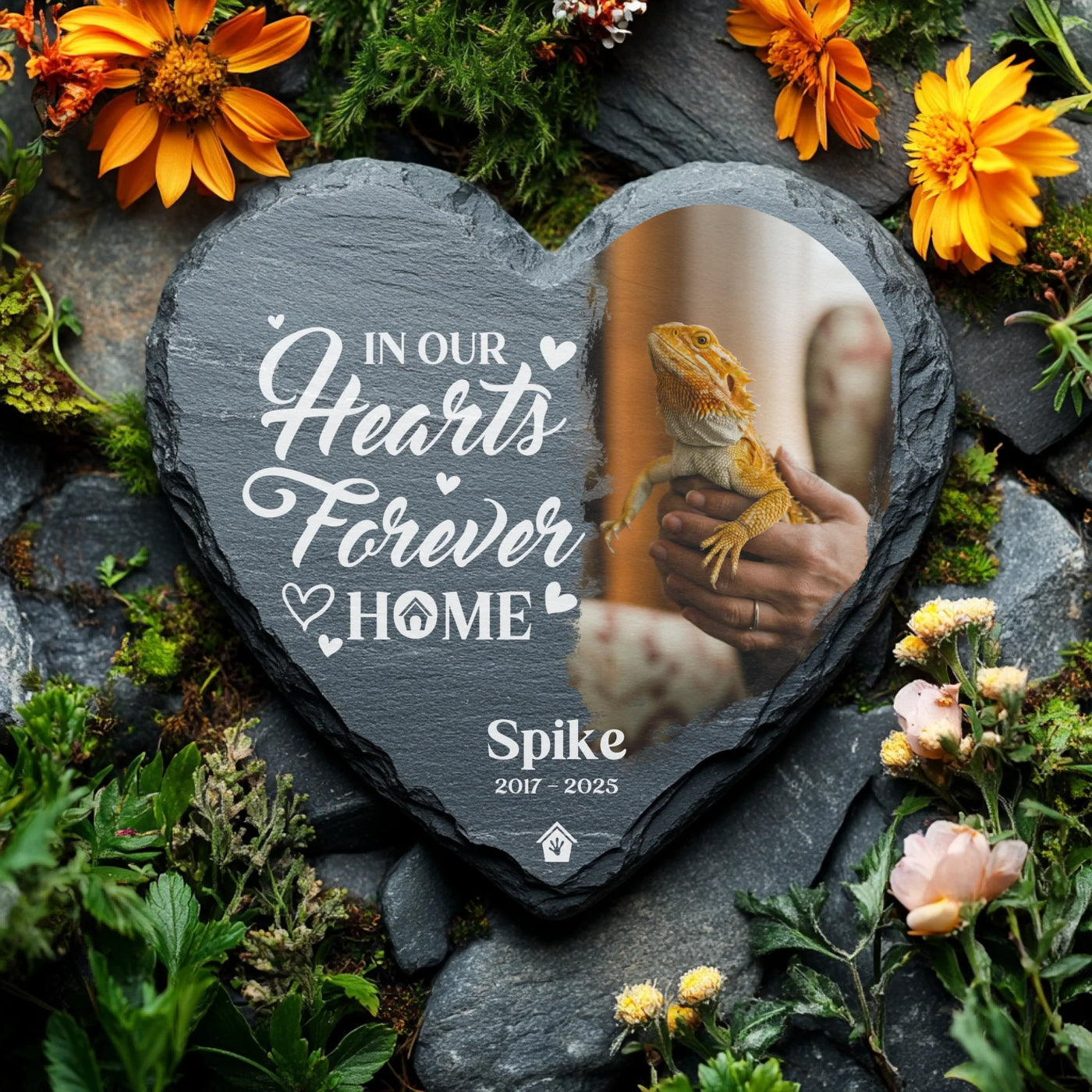 Engraved slate memorial stone for pet lizard Spike, displayed in a flower-filled garden setting with vibrant petals and natural rocks.