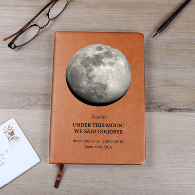 Flat lay: personalized moon-phase journal with gift tag — saddle vegan leather, custom name, date, and location