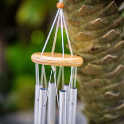 Top section of wind chime showing wooden ring and hanging tubes against a blurred green background