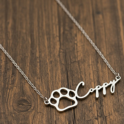 Silver necklace with paw print design and name on a wooden surface