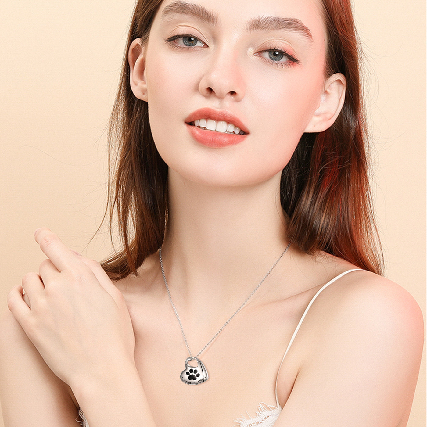 Woman wearing a silver necklace with a paw print pendant on a beige background
