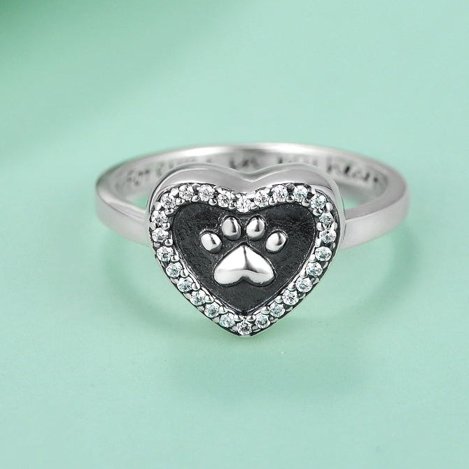 Heart-shaped ring with paw print design on a light green background