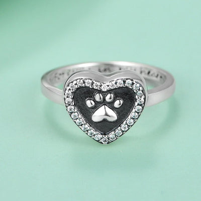 Heart-shaped ring with paw print design on a light green background