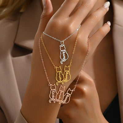 Hand wearing multiple necklaces with cat-themed pendants on a neutral background