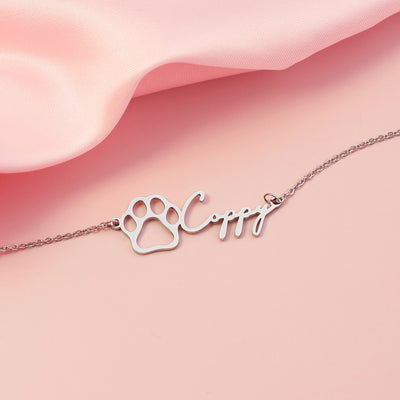 Silver paw print bracelet with a pet  name on a pink fabric background