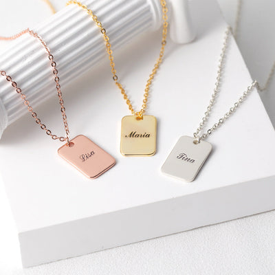 Three necklaces with engraved name tags on a white surface