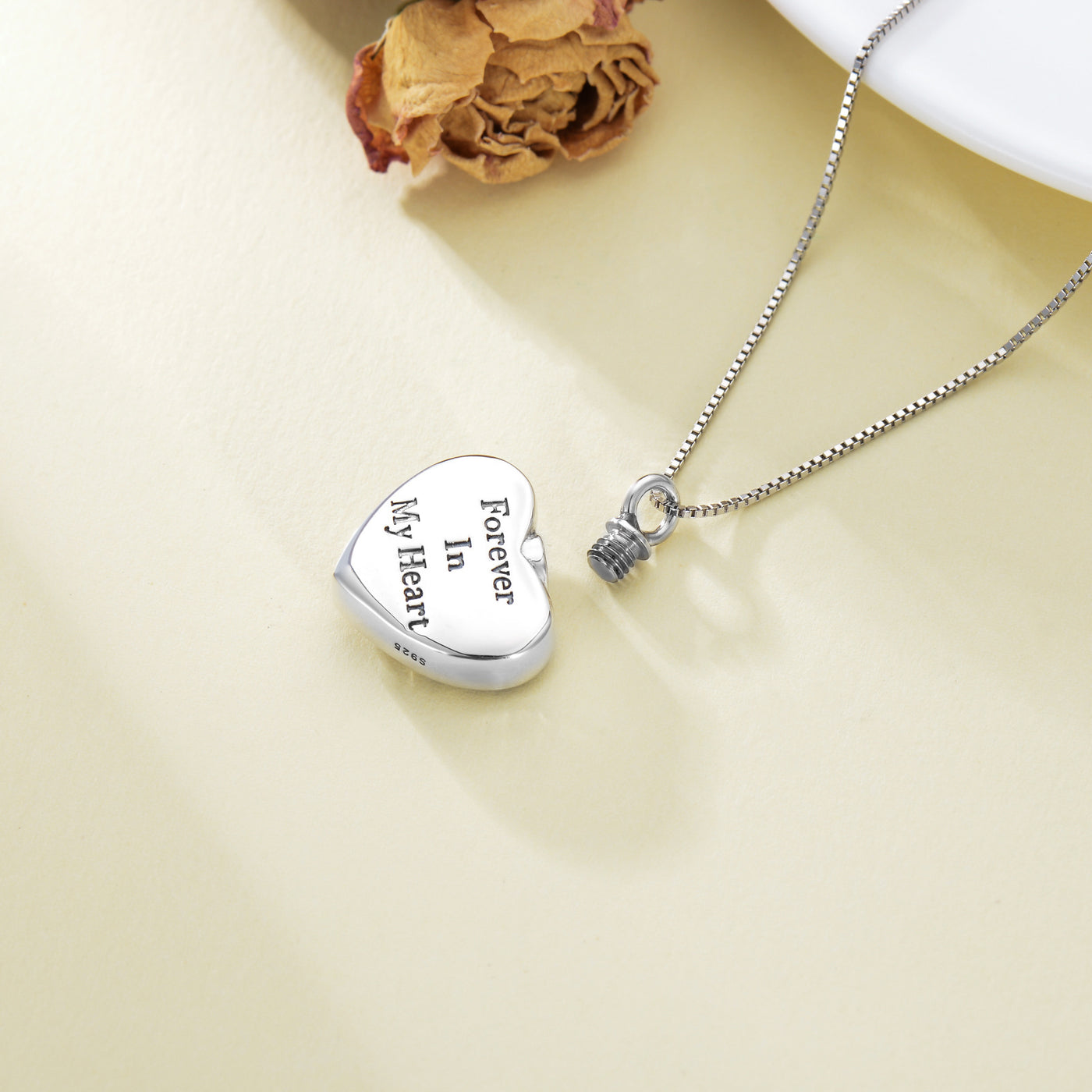 Silver heart-shaped locket with engraved text on a beige background