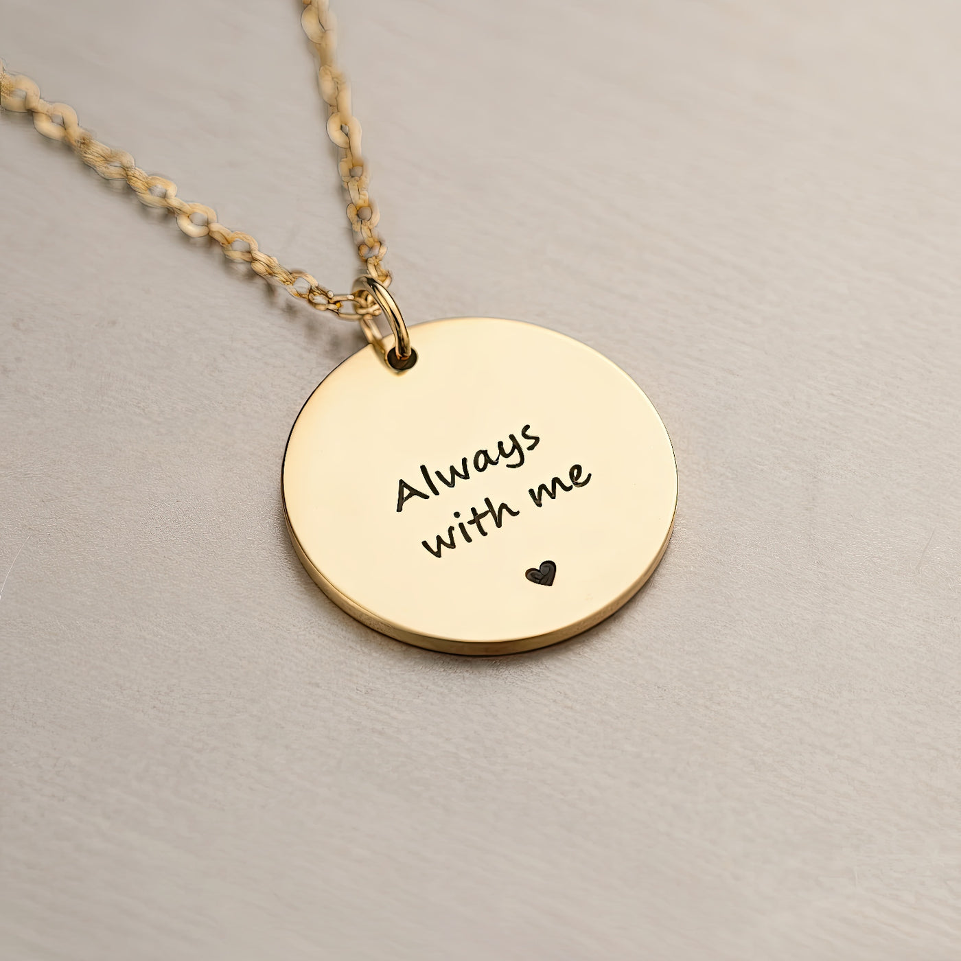 Gold necklace with a round pendant that says 'Always with me' on a beige background