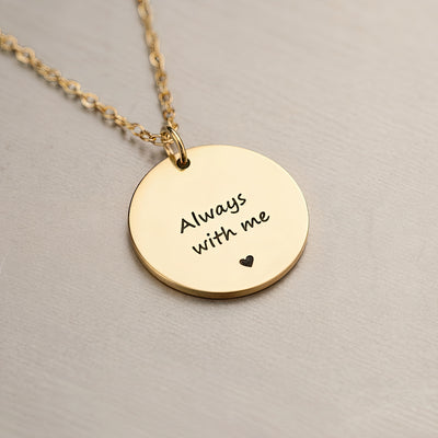 Gold necklace with a round pendant that says 'Always with me' on a beige background