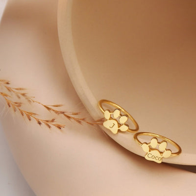 Gold ring with cat paw design on a beige surface