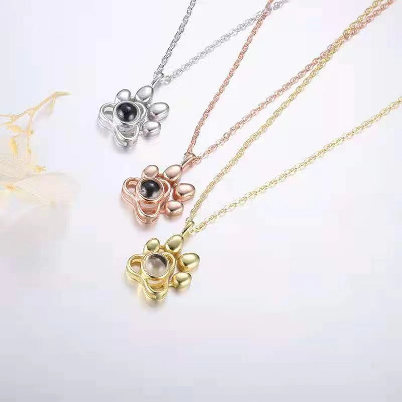 Three paw-shaped necklaces in gold, rose gold, and silver on a white background.