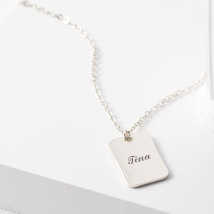 Silver necklace with a tag engraved with 'Tina' on a white surface.