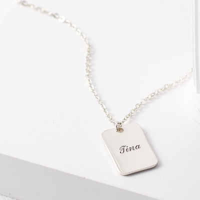 Silver necklace with a tag engraved with 'Tina' on a white surface.