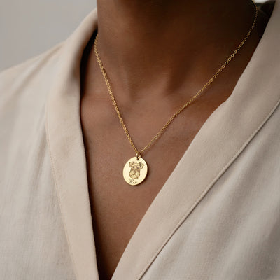 Gold necklace with a pendant worn by a person in a beige outfit